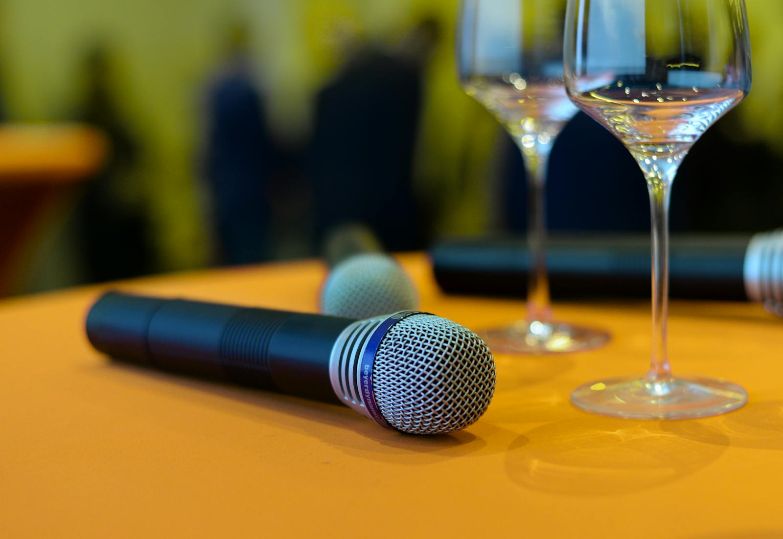 Close-up of microphones and wine glasses on an orange table, ideal for events or entertainment themes.